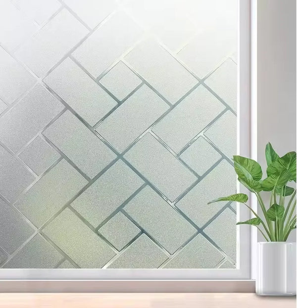 Frosted electrostatic window film applied to a glass pane, featuring a geometric pattern and a green plant in the foreground.