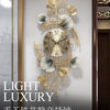A gold-toned metal wall clock featuring decorative ginkgo leaves and a round face, mounted on a light gray wall.