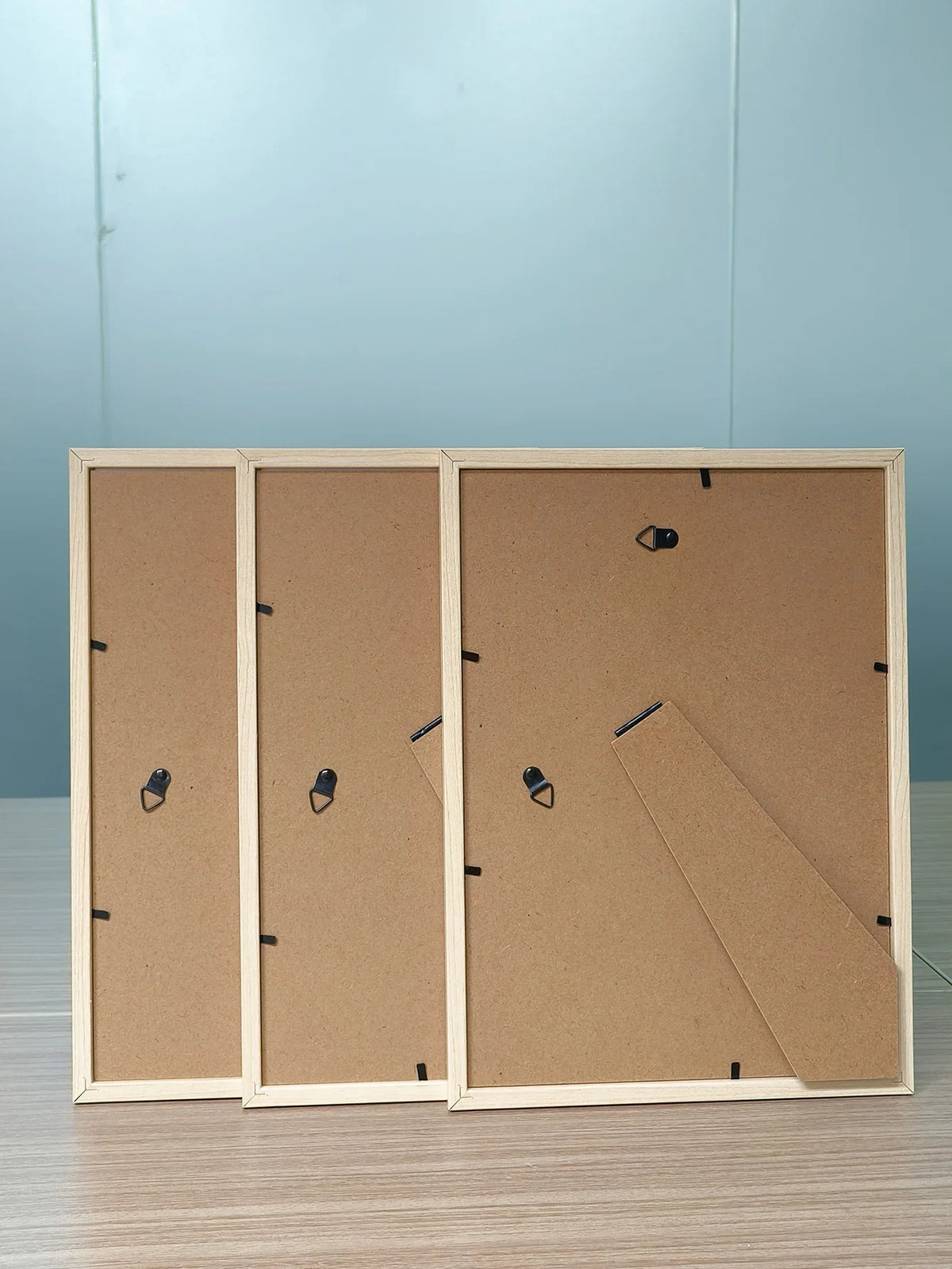 Three solid wood picture frames with acrylic fronts displayed against a light blue background.