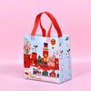 A light blue non-woven gift tote bag with a red handle and festive Christmas holiday prints.