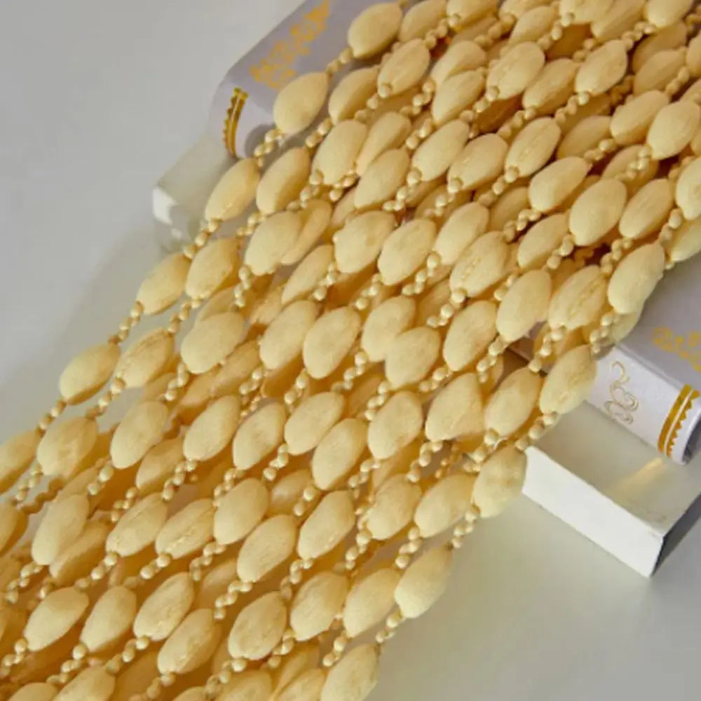 A close-up of a long string curtain made of small, light yellow or beige beads and tassels.