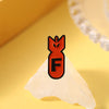 An enamel pin featuring an orange shark design on a white, triangular background.