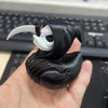A black fabric statue of a duck with a skull face and a white horn, held in a hand against a keyboard background.