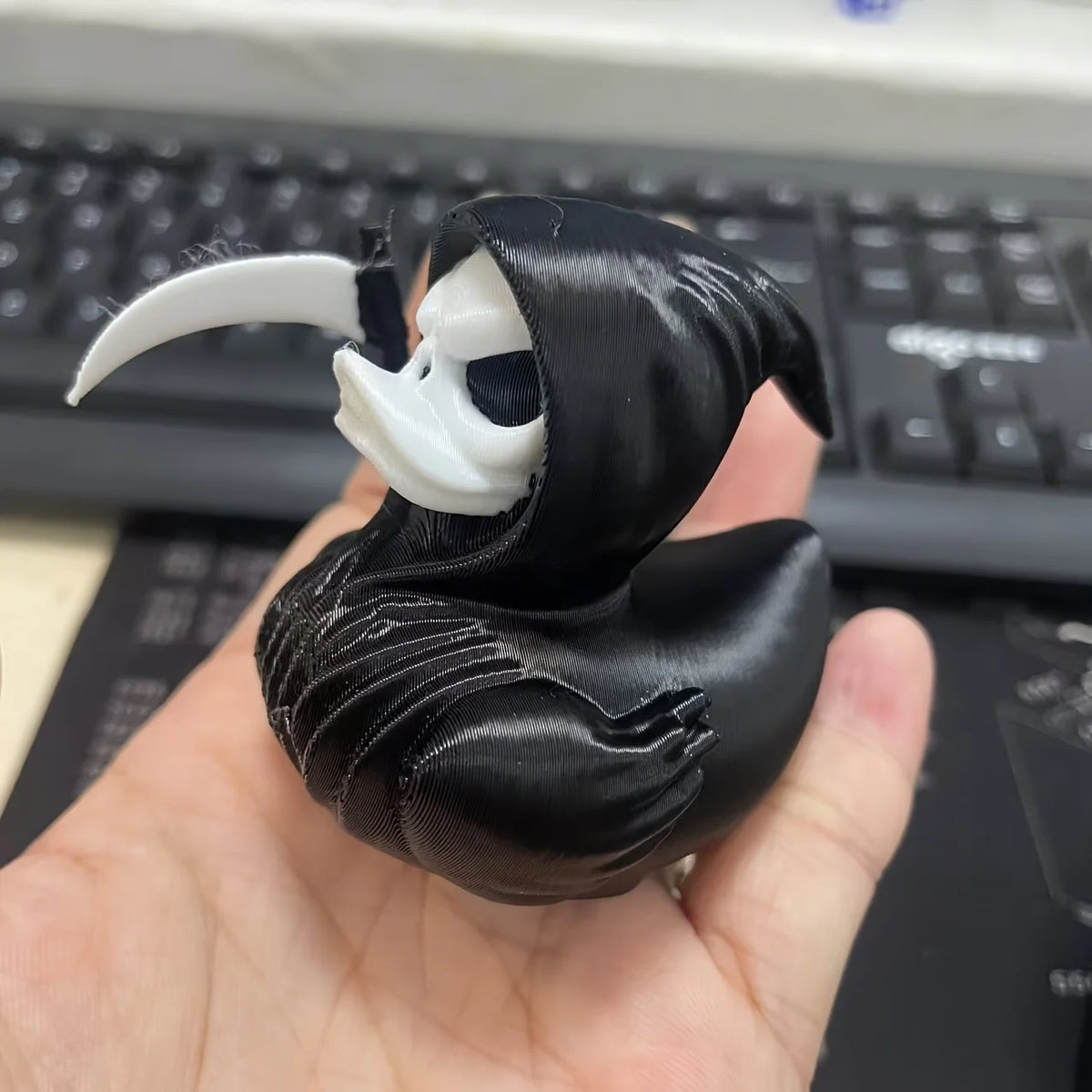 A black fabric statue of a duck with a skull face and a white horn, held in a hand against a keyboard background.