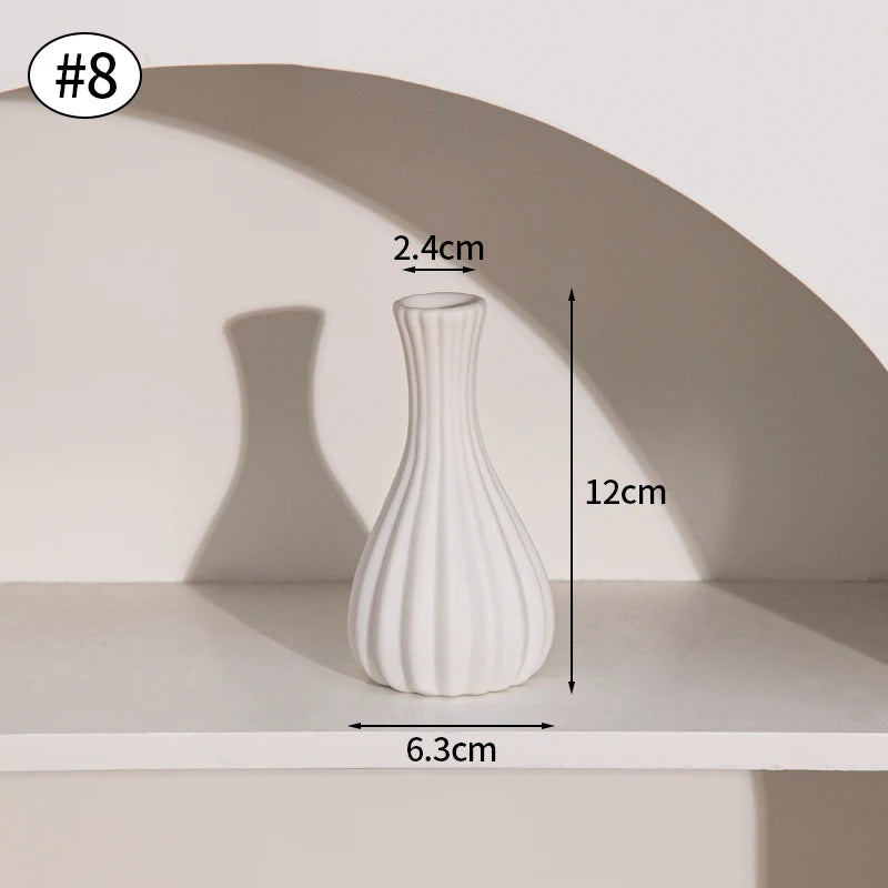A white ceramic bud vase with a fluted design is shown on a shelf, casting a shadow.