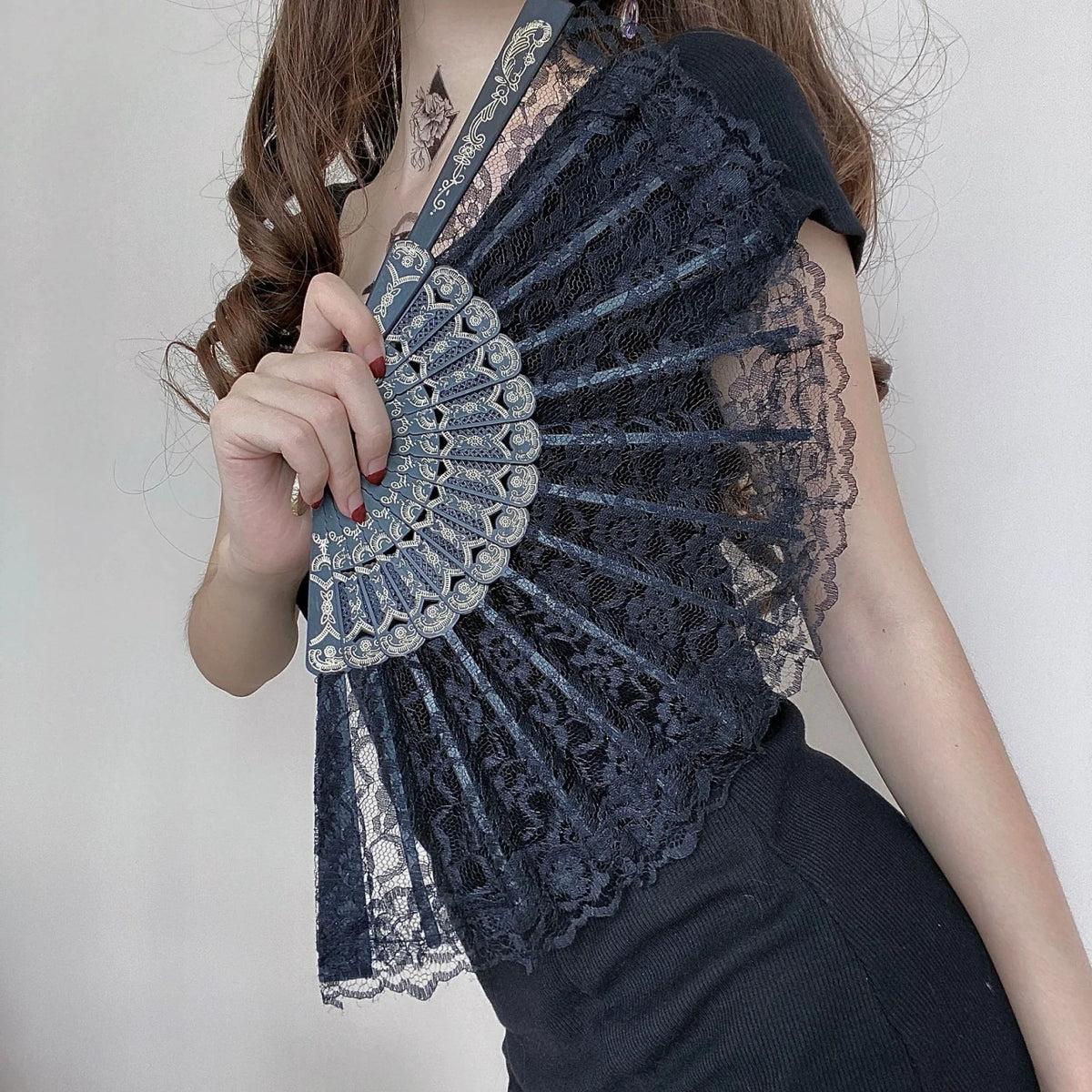 Una mujer modela un abanico de mano de encaje azul oscuro doblado usado como top, con intrincados detalles de ojales y encaje
