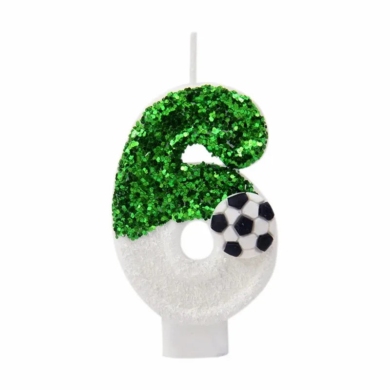 A white candle shaped like the number 6, decorated with green glitter and a black soccer ball detail.