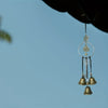 A decorative witch bell wind chime hangs from a dark object against a clear blue sky.