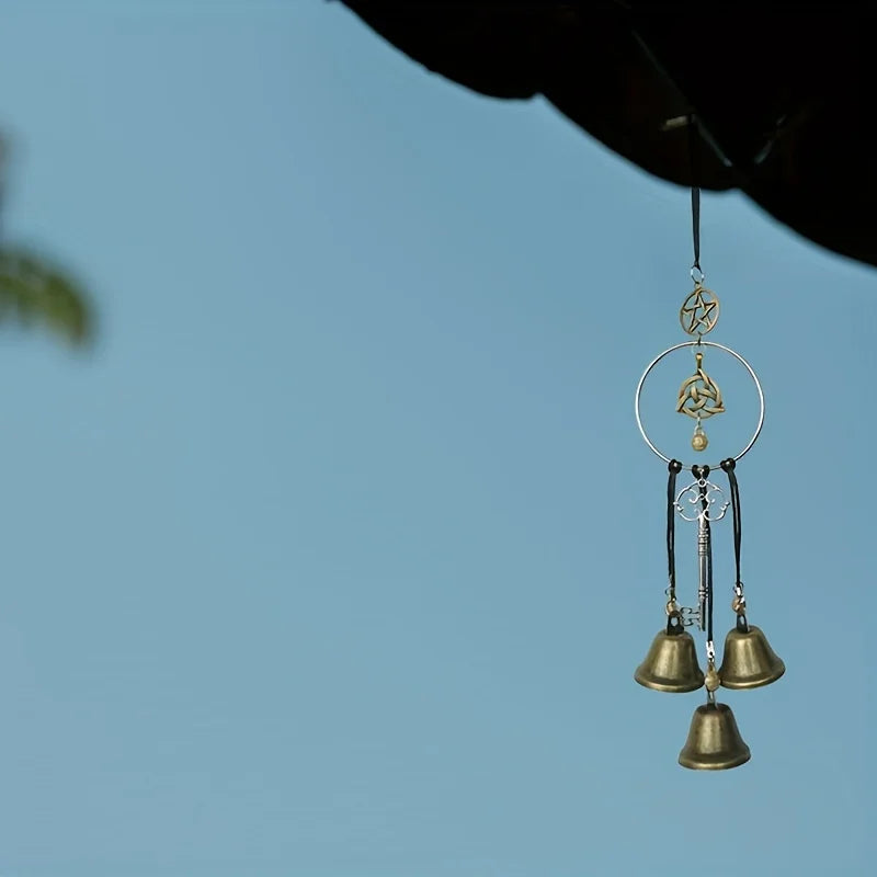 A decorative witch bell wind chime hangs from a dark object against a clear blue sky.