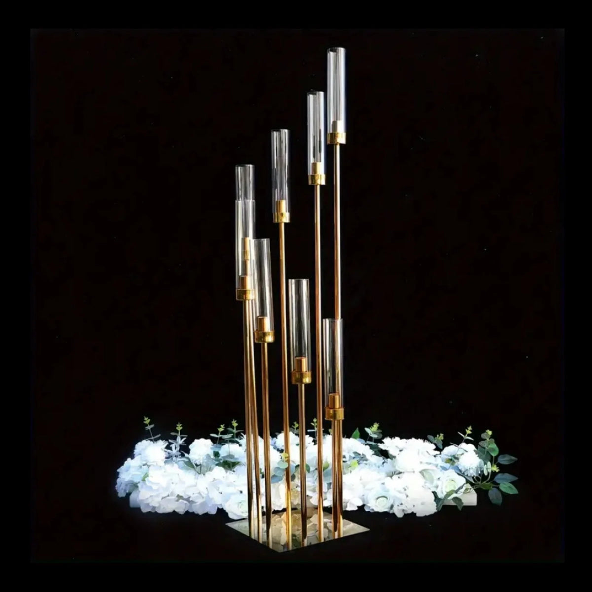 A vertical arrangement of elegant gold metal candle holders with clear glass tubes, set against a dark background and surroun