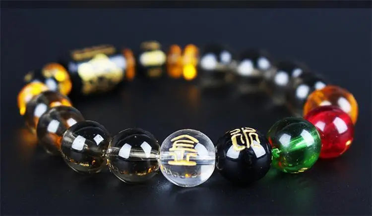 A bracelet made of polished crystal beads, featuring gold and colored stones, laid on a dark surface.