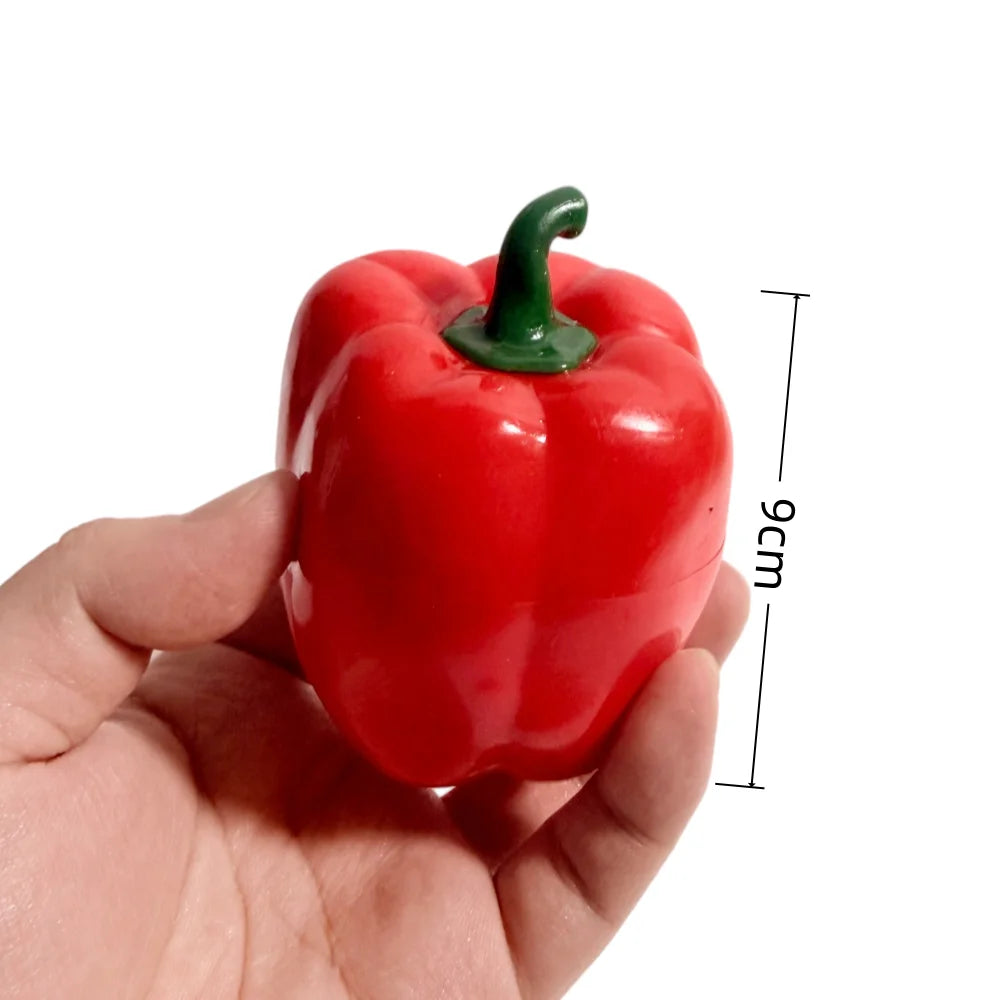 A hand holds a bright red, squishy bell pepper stress relief block with a green stem.