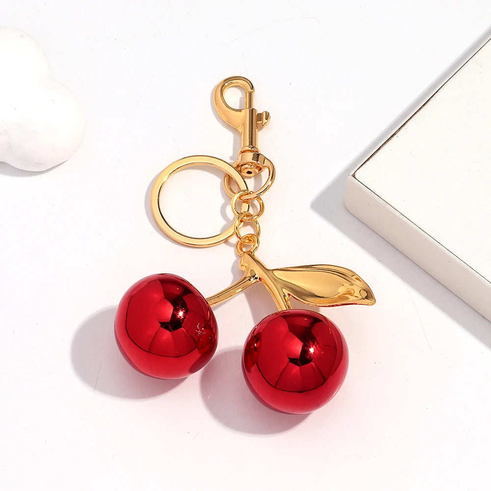 Gold-colored pendant keychain featuring a red cherry resin charm on a white background.