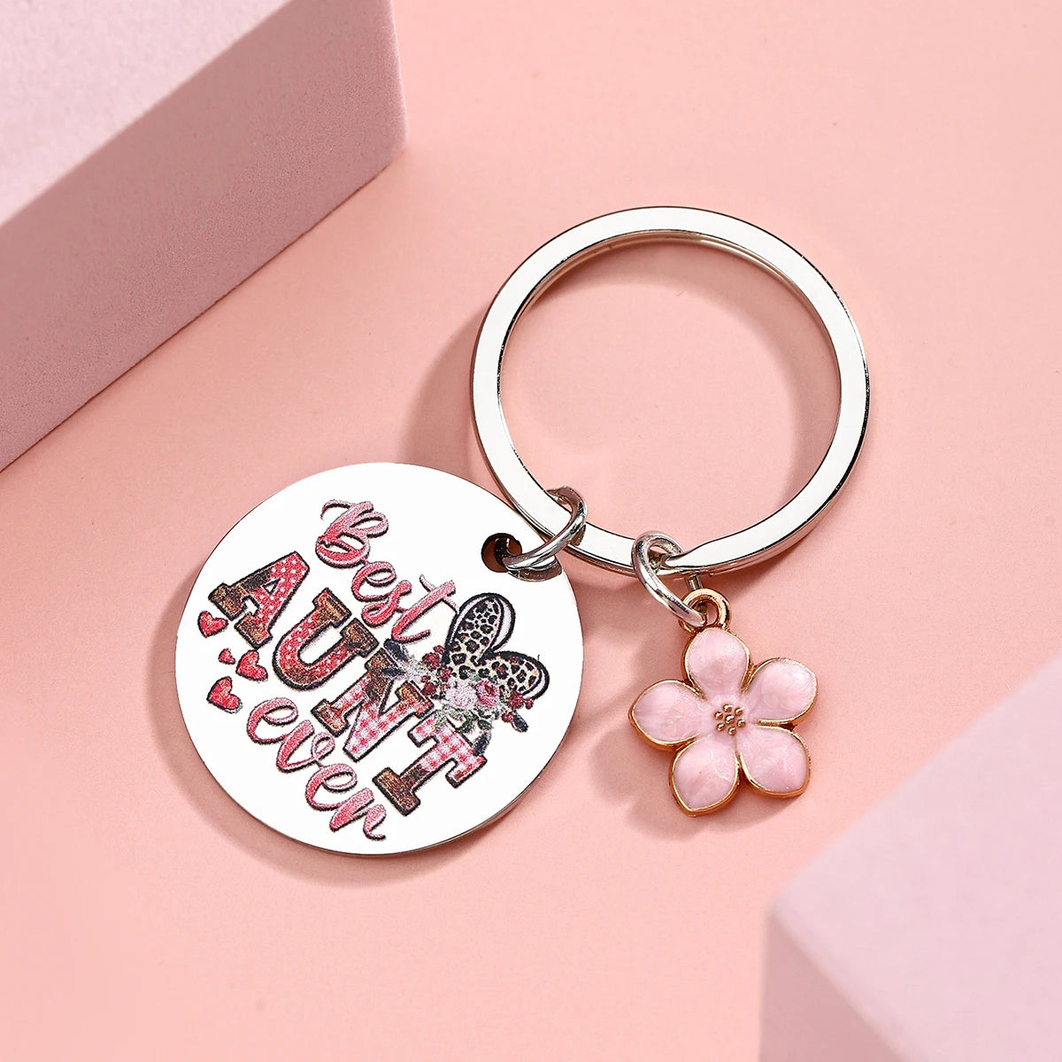 Silberne Edelstahl-Anhänger mit kreisförmigem Charm, der den Text „Best Aunt ever“ und eine rosa Blume zeigt.