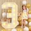 A large, illuminated letter E balloon decoration surrounded by yellow and white balloons for a party.
