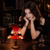 A dark-haired woman holds a red and orange stained glass witch hat night light on a wooden table.