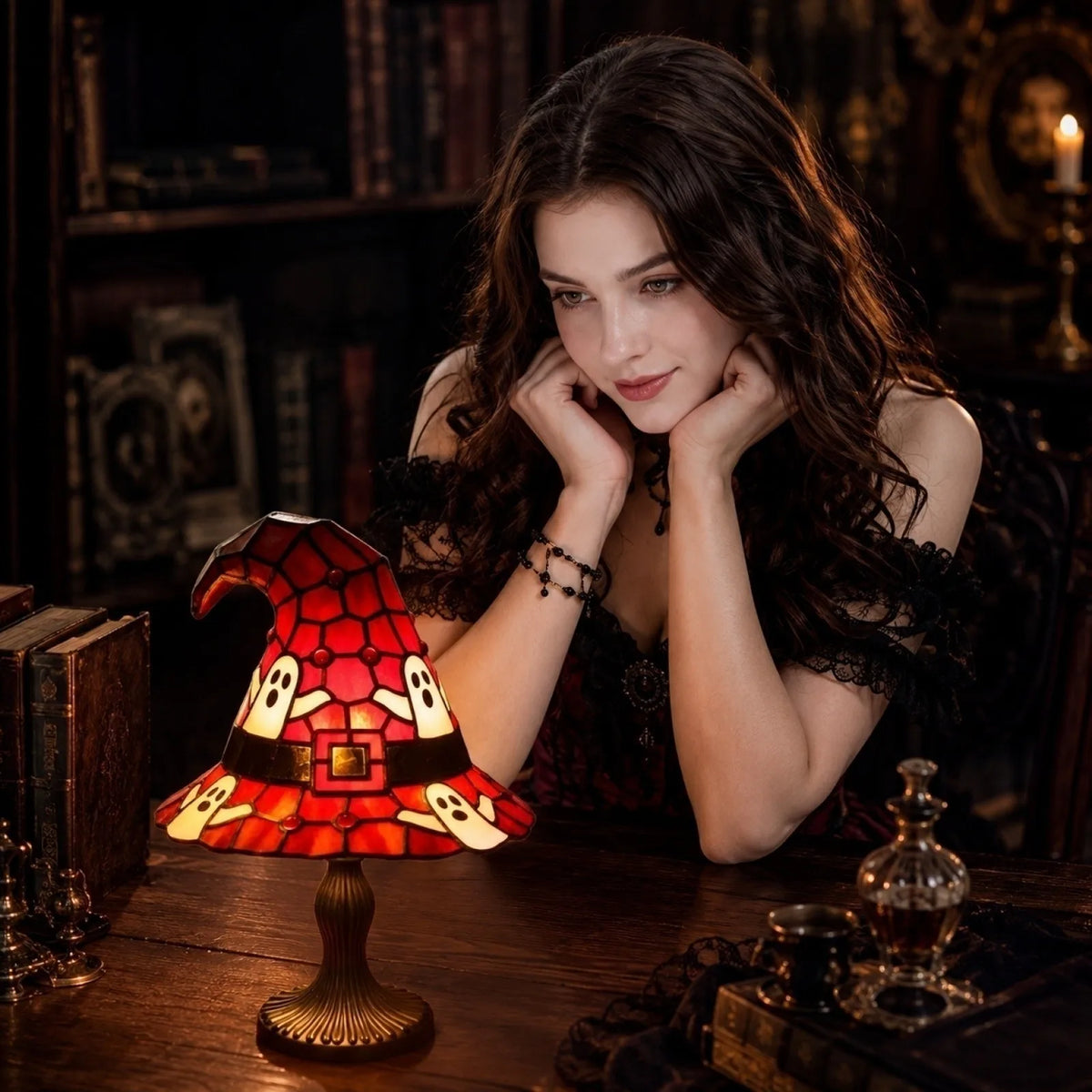 A dark-haired woman holds a red and orange stained glass witch hat night light on a wooden table.