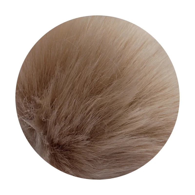 A round pom pom made of light brown faux fur with a silver chain attached.