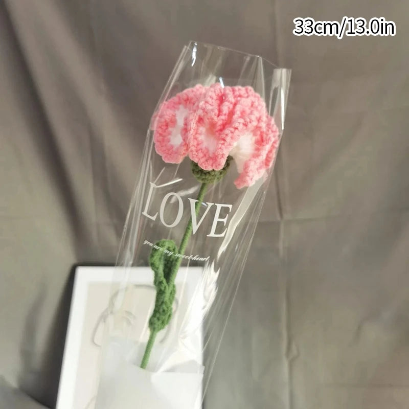 A clear plastic bag containing a handmade pink crochet tulip bouquet with green stems and the word LOVE written on the stem.
