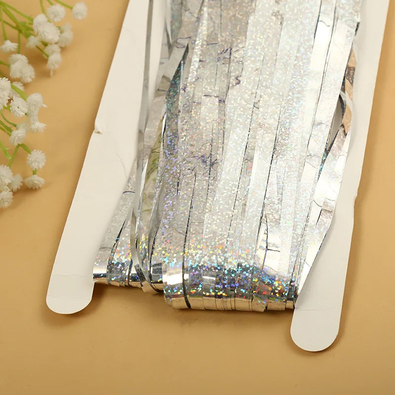 Silver metallic tinsel foil fringe curtain backdrop for parties displayed on a light brown surface.