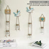 Three decorative glass terrariums with bird-shaped elements hanging on a white wall