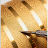 A close-up of metallic gold striped peel-and-stick wallpaper with a silver blade touching the surface.