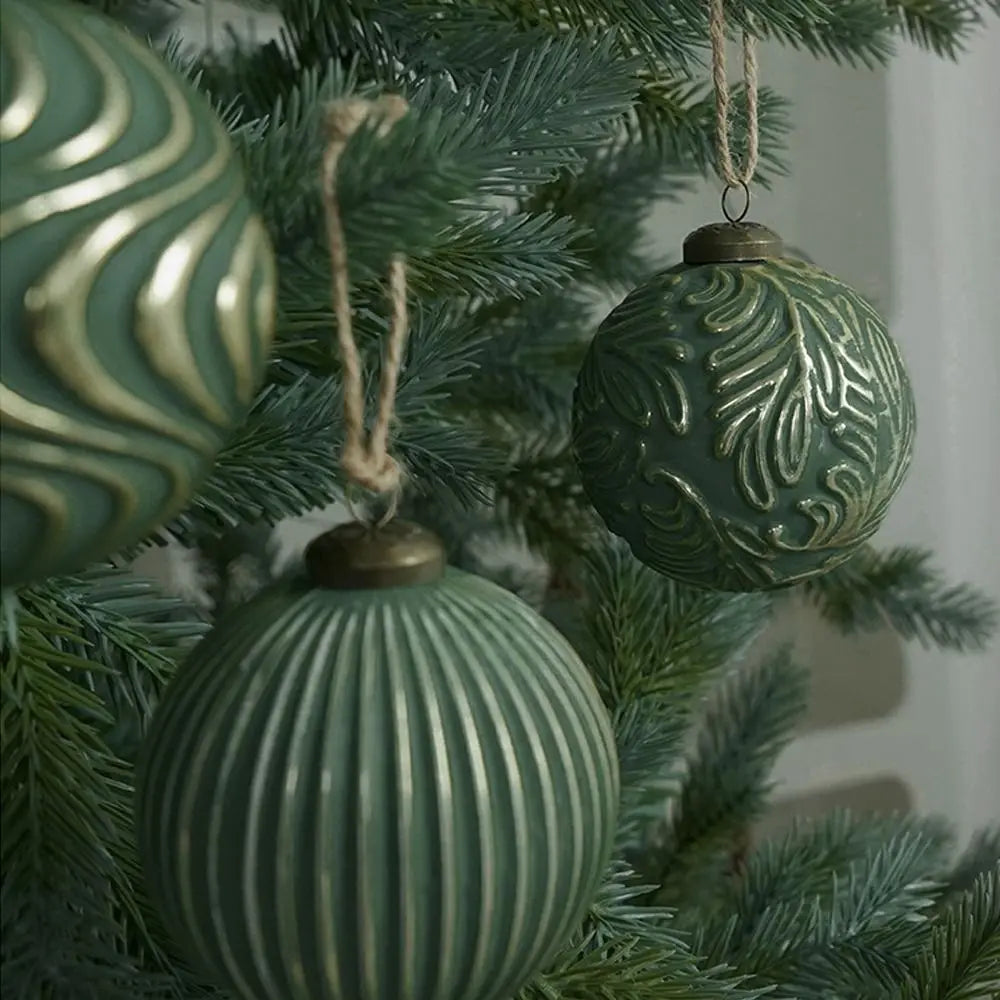 Green glass Christmas tree ornaments hanging on a pine branch.