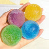 Hand holding four colorful sensory stress reliever squeeze balls: purple, yellow, blue, and green.