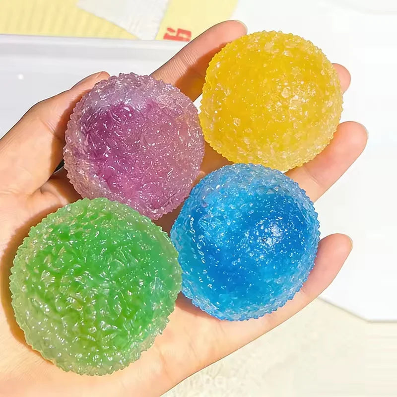 Hand holding four colorful sensory stress reliever squeeze balls: purple, yellow, blue, and green.