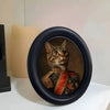 A dark wooden photo frame featuring a portrait of a tabby cat wearing a textured collar and red fabric.
