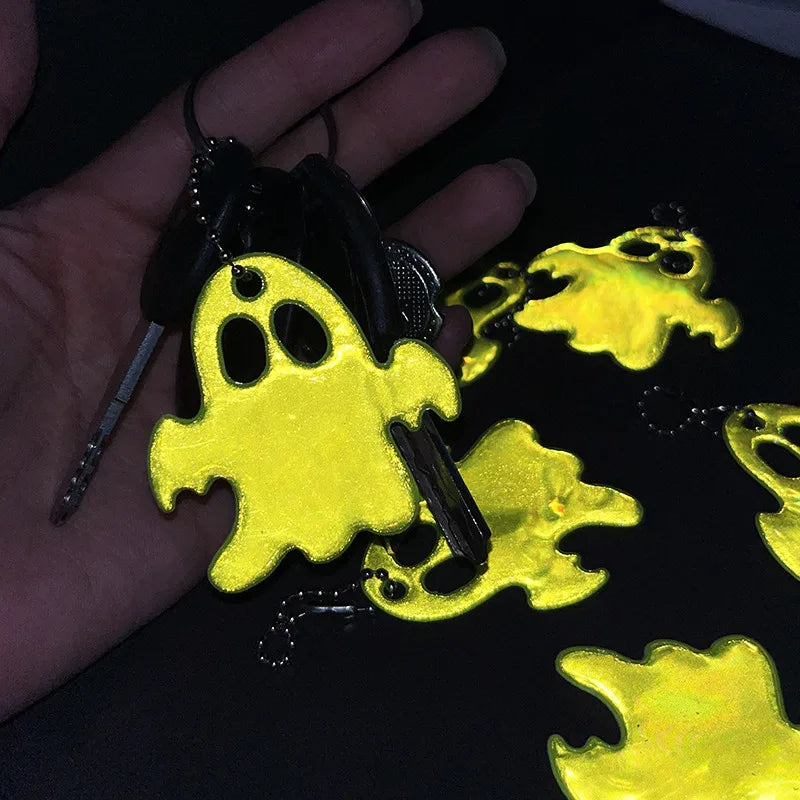 A hand holds a set of yellow ghost-shaped reflective keychains against a black background.