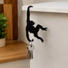 Black monkey-shaped storage hook with a banana design hanging on a white shelf.