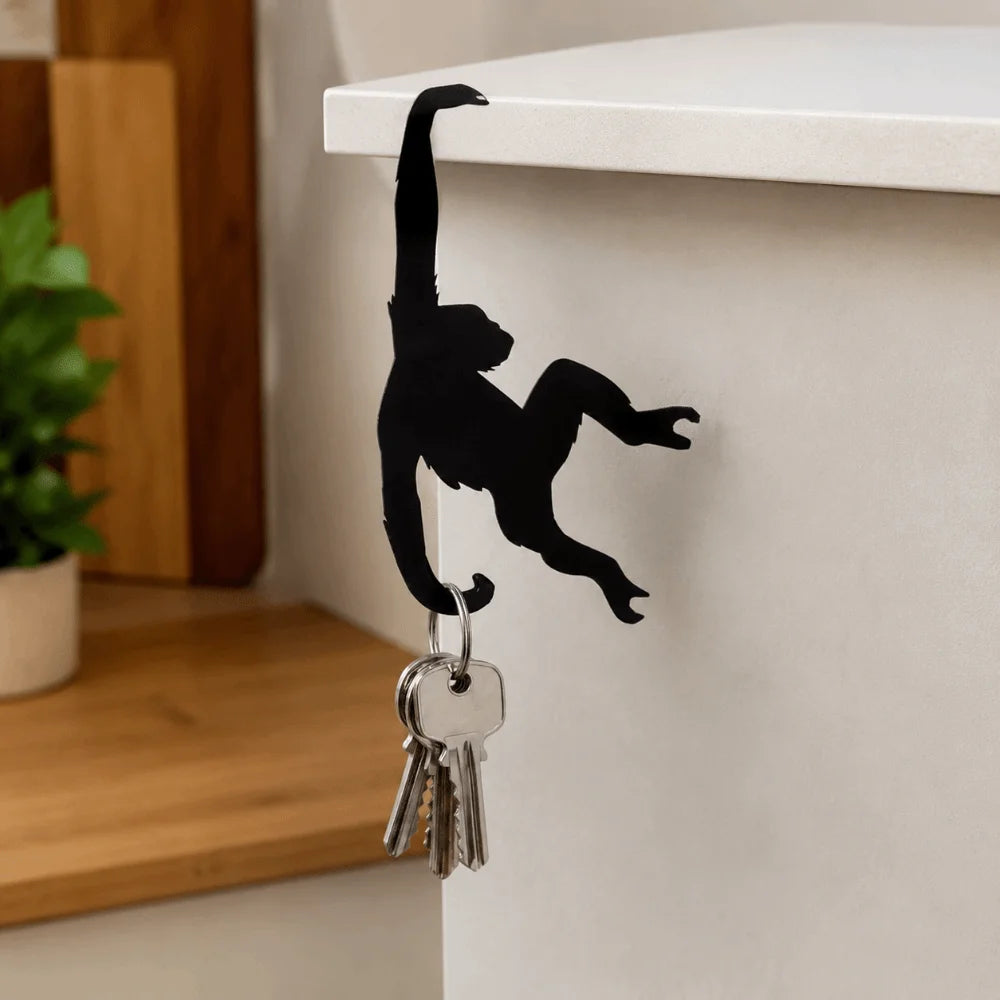 Black monkey-shaped storage hook with a banana design hanging on a white shelf.