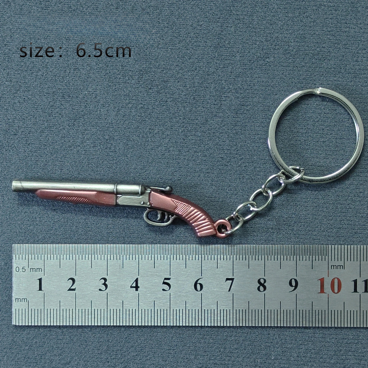 A miniature replica of an alloy gun is attached to a silver keyring, measured against a ruler.
