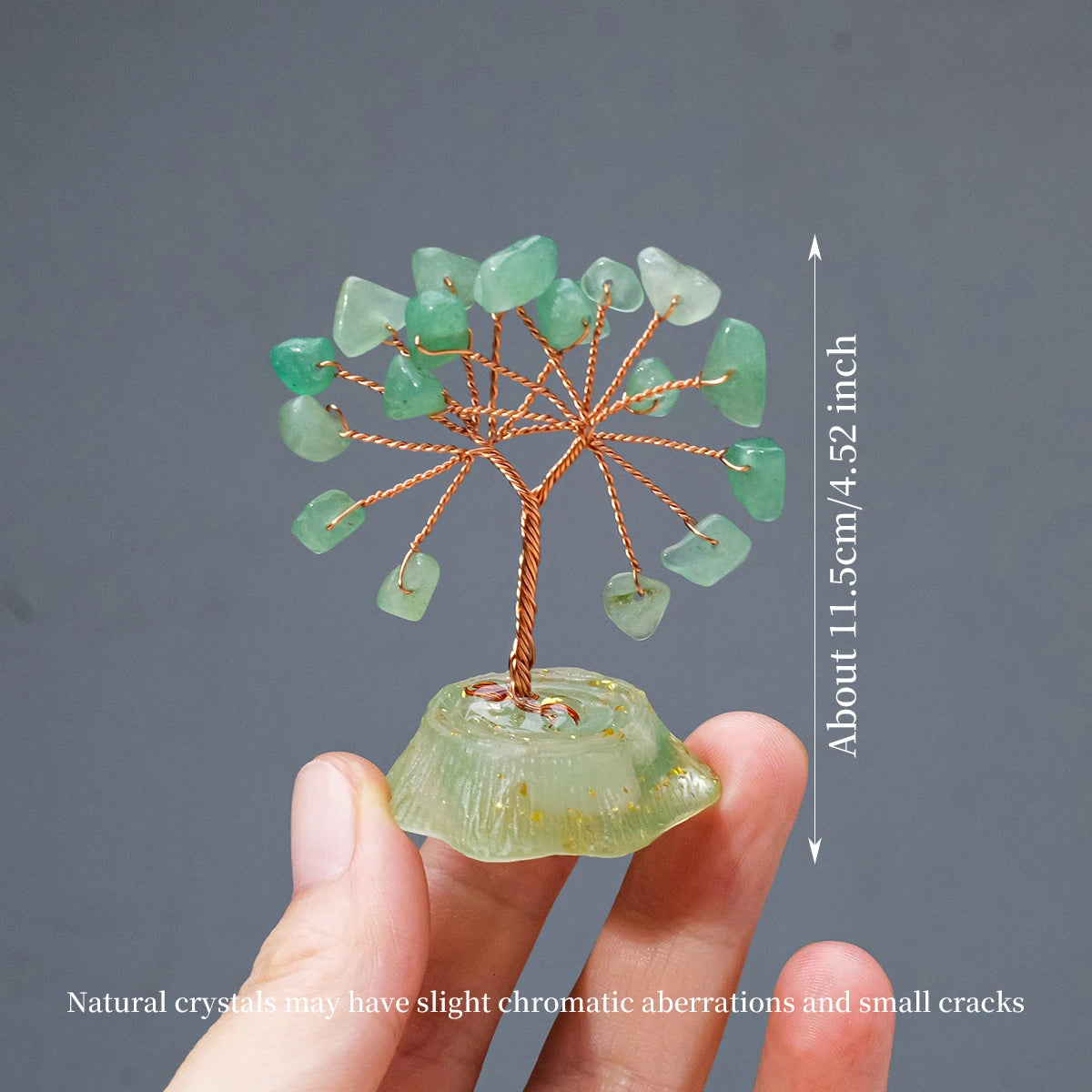 A hand holds a natural crystal tree made of green stones branching out from a larger crystal base.