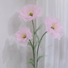 A large artificial silk pink poppy flower with yellow stamens displayed on a green stand against a white background.