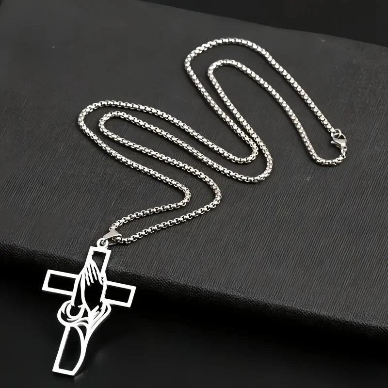 Silver hollow prayer hands cross pendant necklace displayed on a black surface.