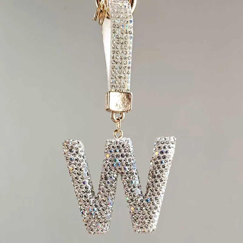 A silver letter charm shaped like a W, encrusted with clear crystals and attached to a chain.