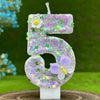 A number cake candle shaped like the number 5 decorated with purple and pink flowers and a small yellow butterfly