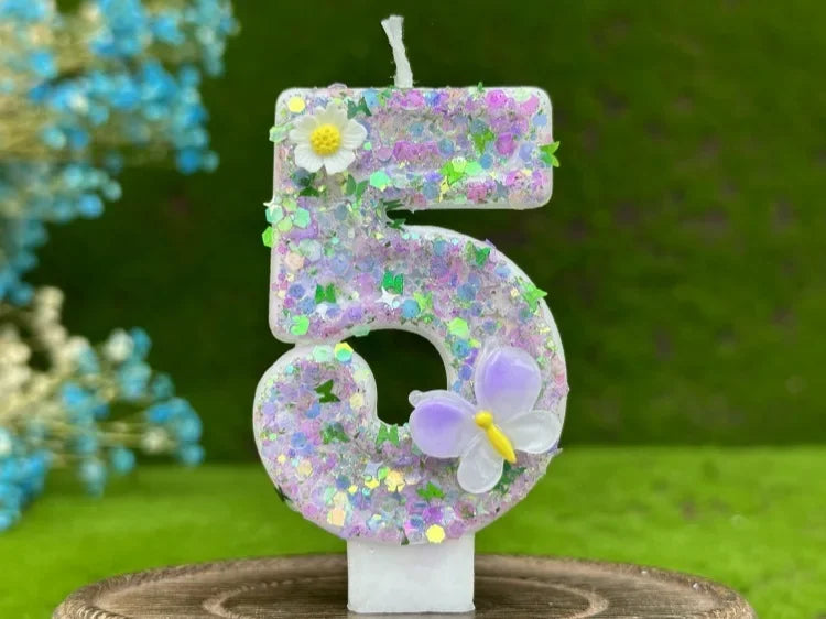 A number cake candle shaped like the number 5 decorated with purple and pink flowers and a small yellow butterfly
