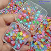 A hand holds two clear plastic containers filled with colorful glow-in-the-dark resin turtle figurines for crafts.