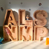 Wooden alphabet letters spelling ALSMP carved from light wood with small decorative elements