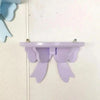 A light purple decorative bow-shaped wooden wall shelf mounted on a white surface.