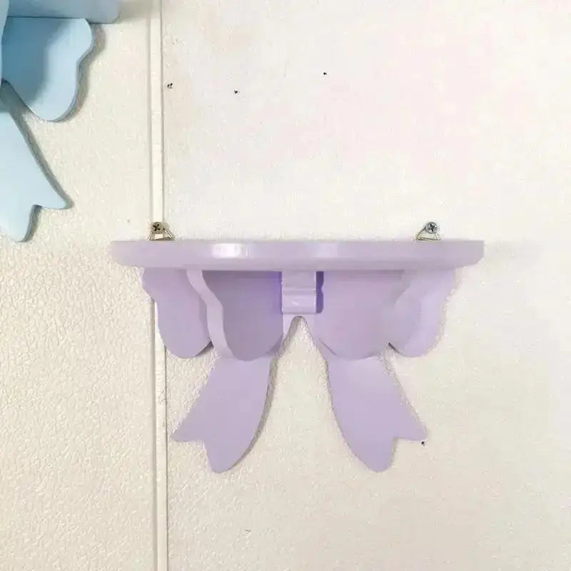 A light purple decorative bow-shaped wooden wall shelf mounted on a white surface.
