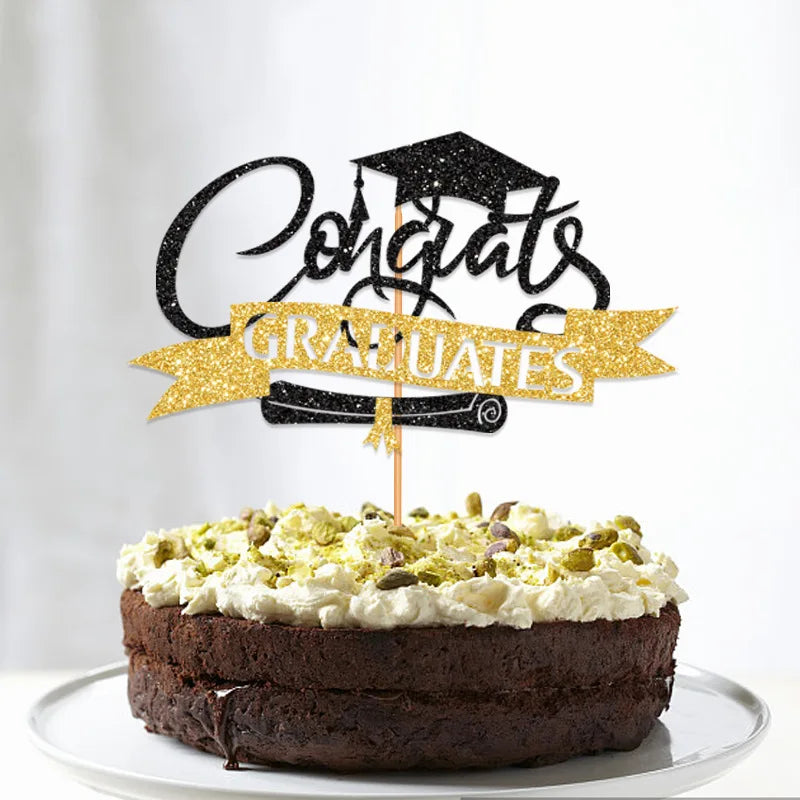 A dark chocolate layer cake decorated with white frosting and topped by black and gold glitter graduation cake toppers.