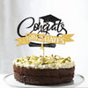A dark chocolate layer cake decorated with white frosting and topped by black and gold glitter graduation cake toppers.