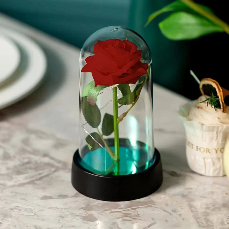 A red rose preserved in a glass dome sits on a black base, displayed on a white surface.