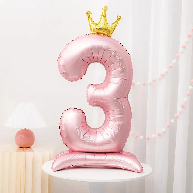 A pink foil number balloon shaped like the number three with a gold crown on top and a stand-up base.