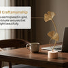 Gold electroplated ginkgo leaf ornament set displayed on a wooden table next to a laptop and a cup.