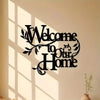 A black metal welcome sign with the text Welcome to Our Home mounted on a light wall, casting shadows.